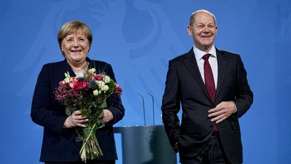 El canciller Olaf Scholz sostiene un ramo de flores durante la despedida de la ex canciller Angela Merkel.