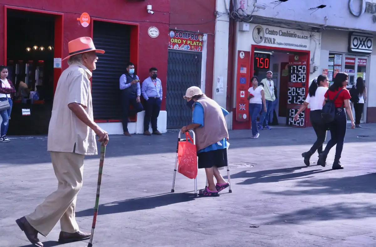 Dos personas de la tercera edad caminan apoyados en un bastón y una andadera en una calle del centro de Cuernavaca.