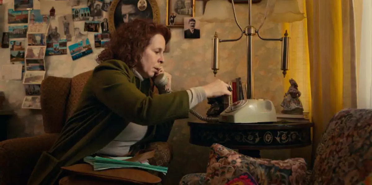 Foto de una escena de la película mexicana 'Corina' en la que la actriz Carolina Politti, quien interpreta a la mamá de la protagonista, está sentada en la salda de su casa y llama por teléfono de disco.