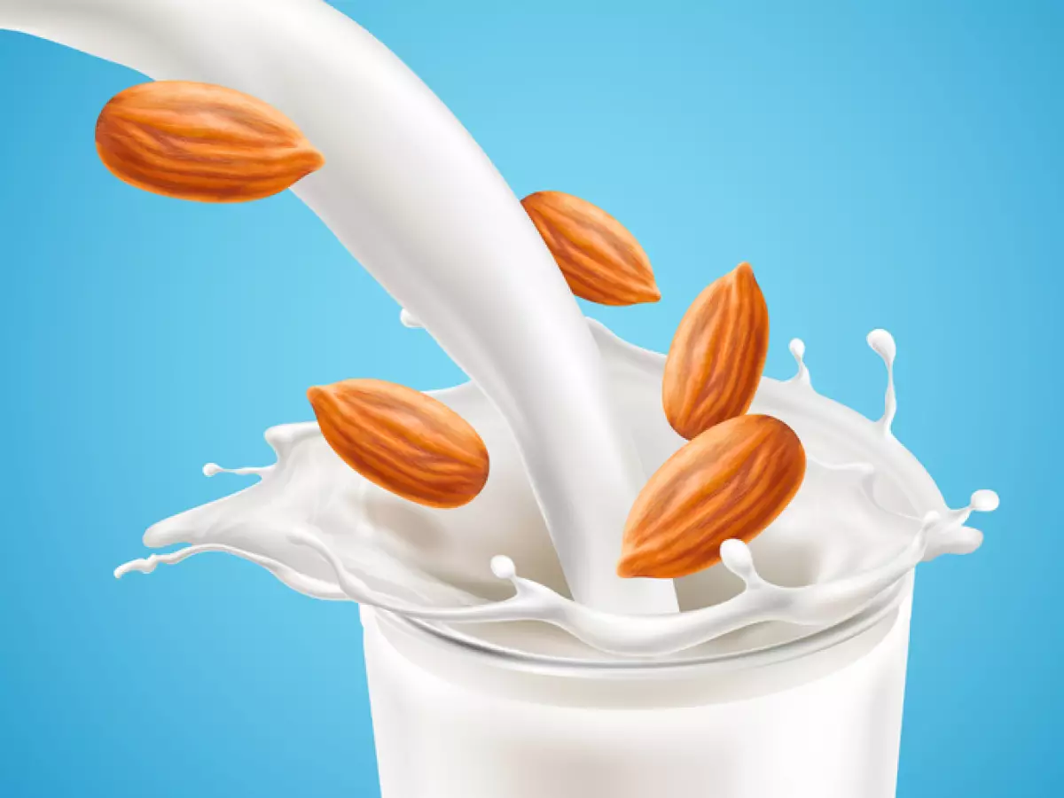 Milk plashing effect with liquid pouring down in glass cup with flying almond kernels isolated on blue background. Design element for advertising beverages. Vector 3d realistic illustration