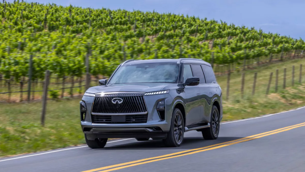 Foto de la camioneta Infiniti QX80 2025 en la carretera con los viñedos de Napa detrás.