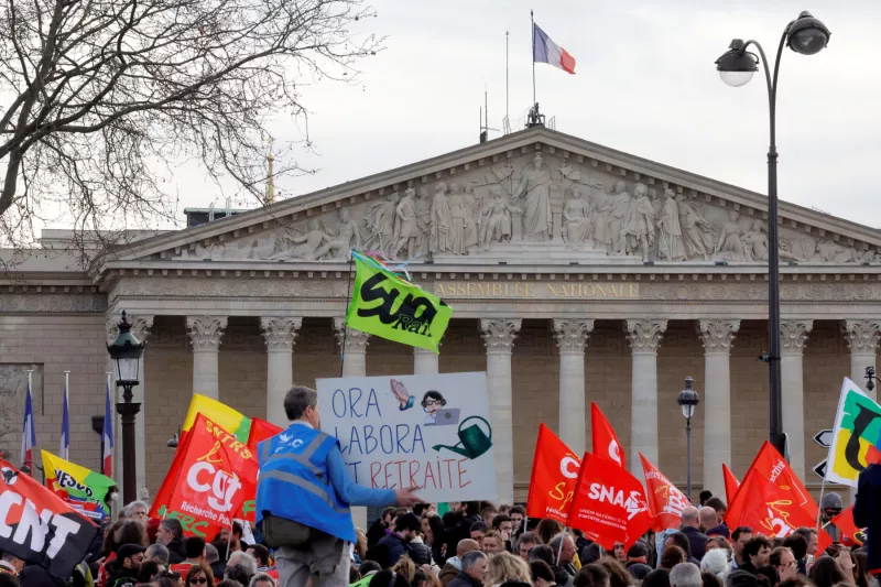 Los manifestantes sostienen pancartas mientras se reúnen en la plaza de la Concordia, cerca de la Asamblea Nacional, para protestar después de que la primera ministra francesa, Elisabeth Borne, pronunció un discurso para anunciar el uso del artículo 49.3, una cláusula especial de la Constitución francesa, para impulsar el proyecto de ley de reforma de las pensiones. a través de la cámara baja del parlamento sin el voto de los legisladores, en París, Francia, el 16 de marzo de 2023.