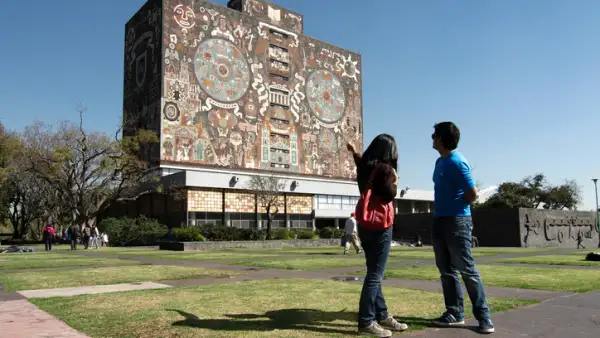 Dos jóvenes estudiantes de la UNAM frente a la Biblioteca Central de Ciudad Universitaria.