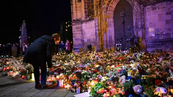 Una mujer se inclina para colocar un homenaje con flores y velas dejadas cerca del mercado navideño "Alter Markt", donde un hombre condujo un automóvil entre la multitud a través de una ruta de salida de emergencia el viernes por la noche, en Magdeburgo, Alemania, el 22 de diciembre de 2024.