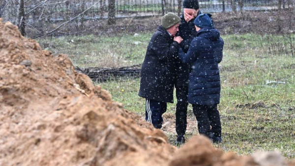 Tres personas se abrazan cerca de una fosa común en la ciudad de Bucha, al noroeste de la capital de Ucrania, Kiev.
