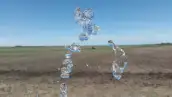 Chorro de agua en primer plano, de fondo un campo a medio sembrar.
