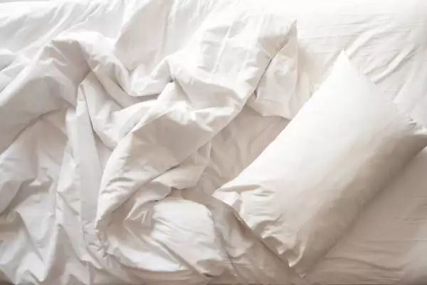  White pillow with blanket on bed unmade.