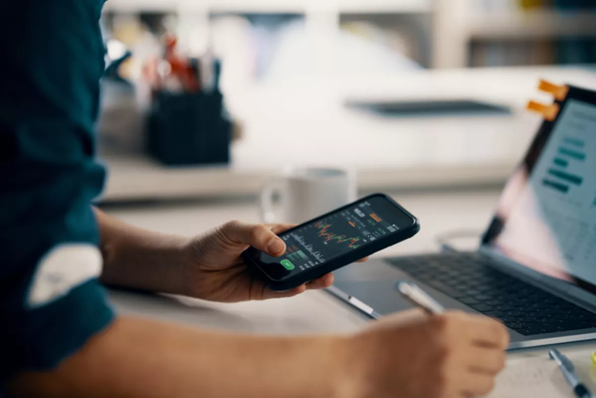 Hombre adulto medio revisando información financiera en un teléfono inteligente mientras hace su contabilidad