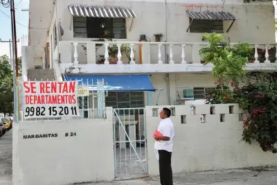 Un hombre parado frente a una casa con un letrero que dice "se rentan departamentos". 