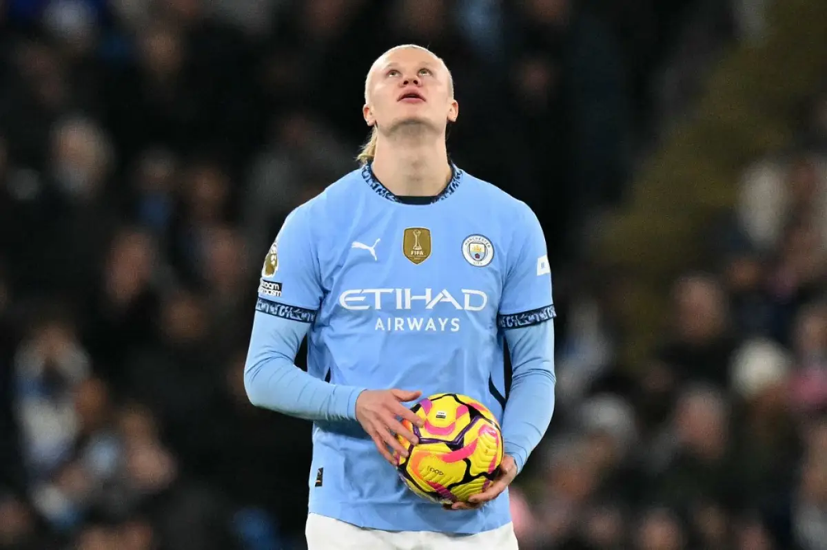 Foto de Erling Haaland con la vista al cielo, vestido con el uniforme azul celeste del Manchester City y un balón entre las manos.