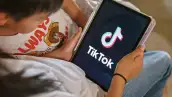 Dos menores de edad miran la pantalla de una tableta donde aparece el logo de TikTok. 