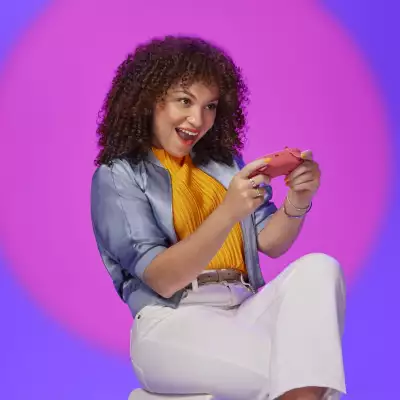 Mujer gamer sentada sosteniendo un control en la mano con una expresión divertida.