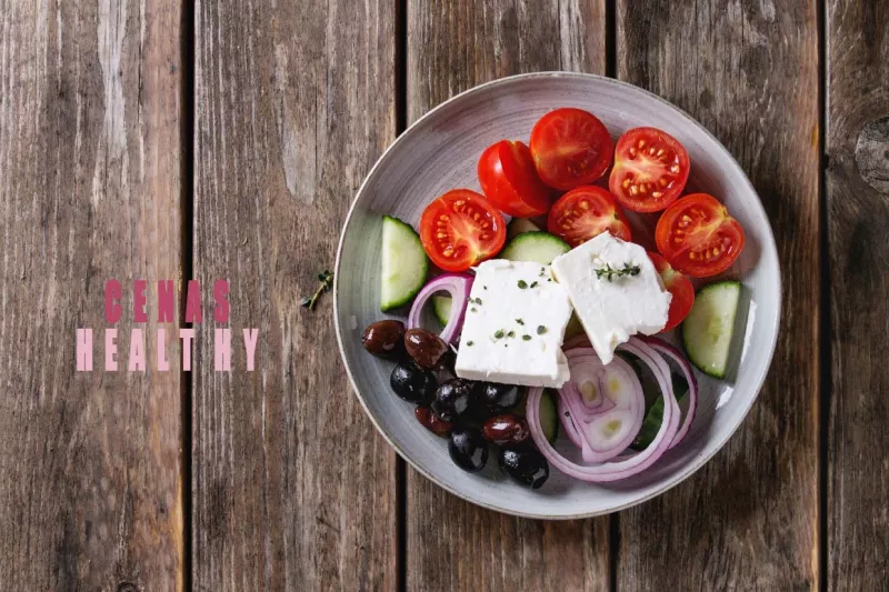Ingredients for traditional greek salad. Cherry tomatoes, sliced cucumbers, red onion, black olives, feta cheese gray ceramic plate over wooden plank background. Top view with copy space