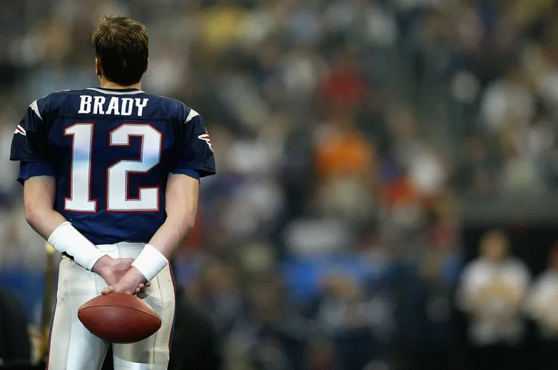 Foto de Tom Brady de espalda y el balón entre las manos con el número 12 en la playera del uniforme de los Patriots de Nueva Inglaterra.