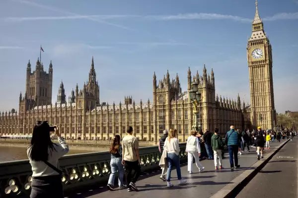 El 12 de abril de 2025, los turistas pasan por las Casas del Parlamento a lo largo del Puente de Westminster en Londres, Inglaterra. Los parlamentarios son llamados a la Cámara de los Comunes para una sesión de emergencia el sábado para debatir el futuro incierto de British Steel en medio de los temores de que el último horno de explosión en funcionamiento de Gran Bretaña en la planta de propiedad china en Sunthorpe pueda cerrar tan pronto como el próximo mes.
