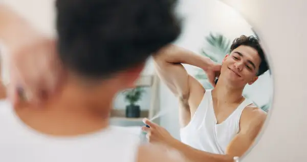 Mirror, man or deodorant in bathroom for hygiene, grooming body or self care in home. Armpit, beauty perfume or reflection of person with fresh scent, spray fragrance or smile with skincare cosmetics