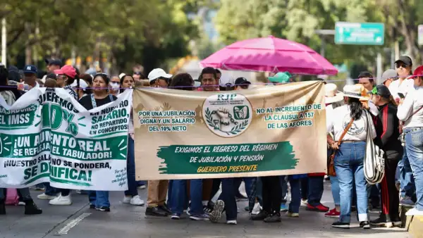 Dos carteles, uno blanco y uno café con verde que portan personas en una avenida con árboles y sombrillas.jpg