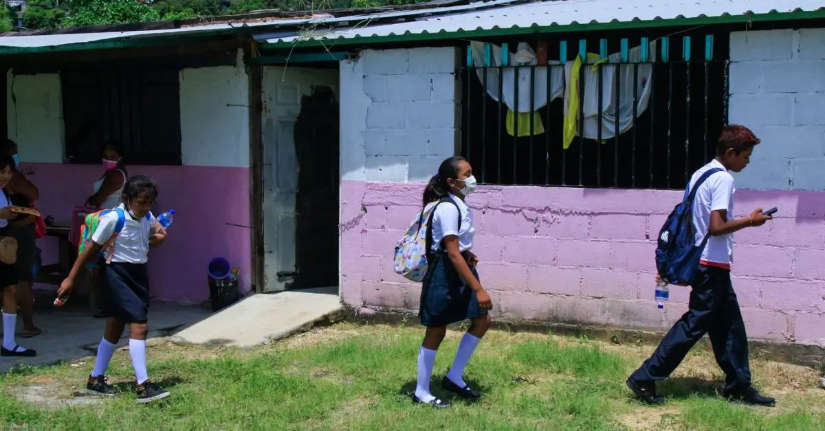 Niñas caminando con uniforme y mochila escolar. 