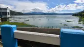 Un cuerpo de agua a cielo abierto; a las orillas hay árboles y una infraestructura en color blanco y azul.jpg