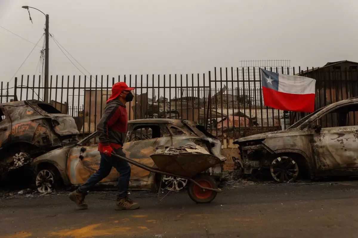 Un residente empuja una carretilla a lo largo de una calle bordeada con los restos carbonizados de vehículos destruidos después de que un incendio forestal devastara Lirquen, una ciudad en Penco cerca de la ciudad de Concepción, Chile, el 20 de enero de 2026. Los bomberos que luchan contra los principales incendios forestales en el sur de Chile que han matado a 20 personas en los últimos cuatro días se beneficiaron del clima más frío a principios del 20 de enero, dijeron las autoridades.
