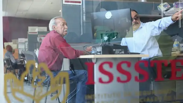Adulto mayor frente a un trabajador del ISSSTE en las oficinas de la dependencia.