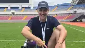 Foto del actor Juan Pablo Medina sonriendo y sentado en un campo de futbol, usa una gorra y muestra su prótesis deportiva.