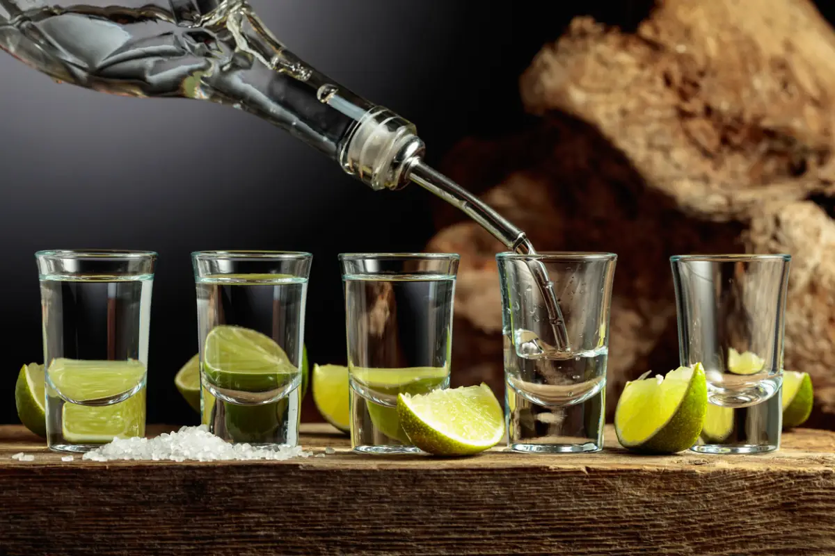 Silver Tequila with salt and lime slices on an old wooden board.