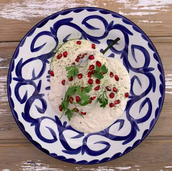 Foto de chile en nogada servido con la salsa (nogada) encima y granos de granada roja.