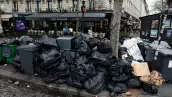 Gente camina en la calle donde los botes de basura están rebasados y la basura no ha sido recolectadas
