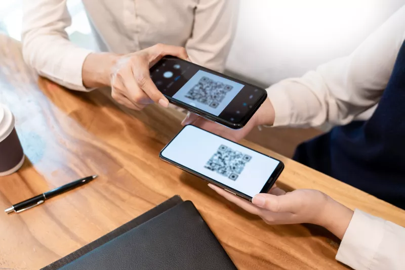 Dos personas sostienen sus celulares con códigos QR en la pantalla para hacer una transacción 