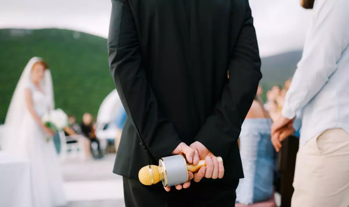 The host at a wedding party stands and holds a microphone behind his back, close-up