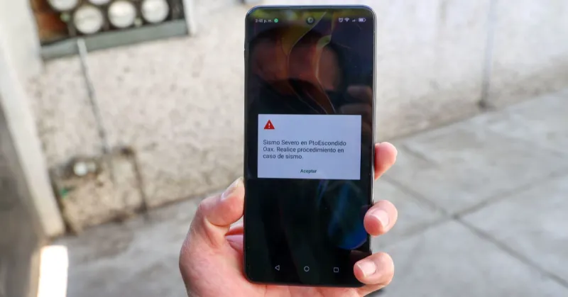 La mano izquierda de una personas sostiene un teléfono celular en donde suena la alerta sísmica.jpg