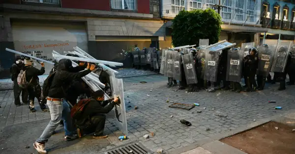 Jóvenes vestidos de negro con toletes frente a policías igual con toletes en una calle, frente a frente.jpg