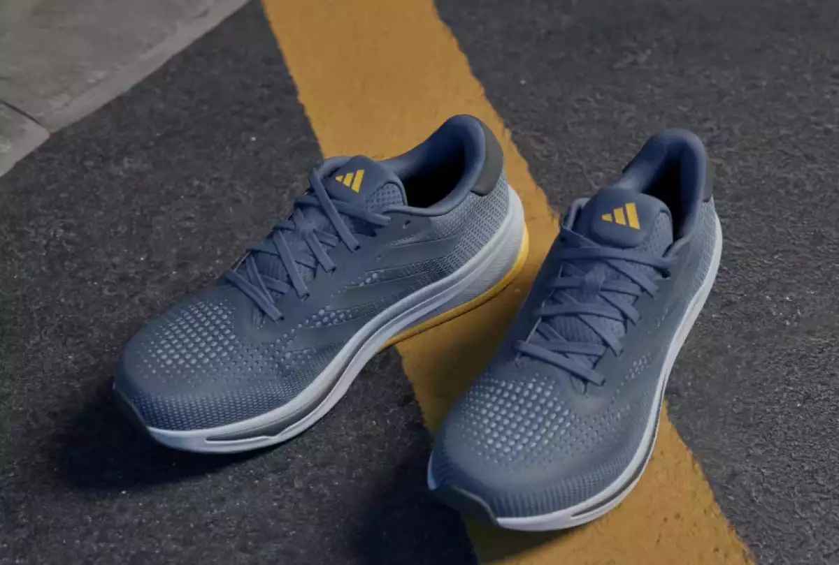 foto de los tenis supernova de adidas especiales para correr en color gris oscuro, con suela gris claro y el logo de la marca en amarillo