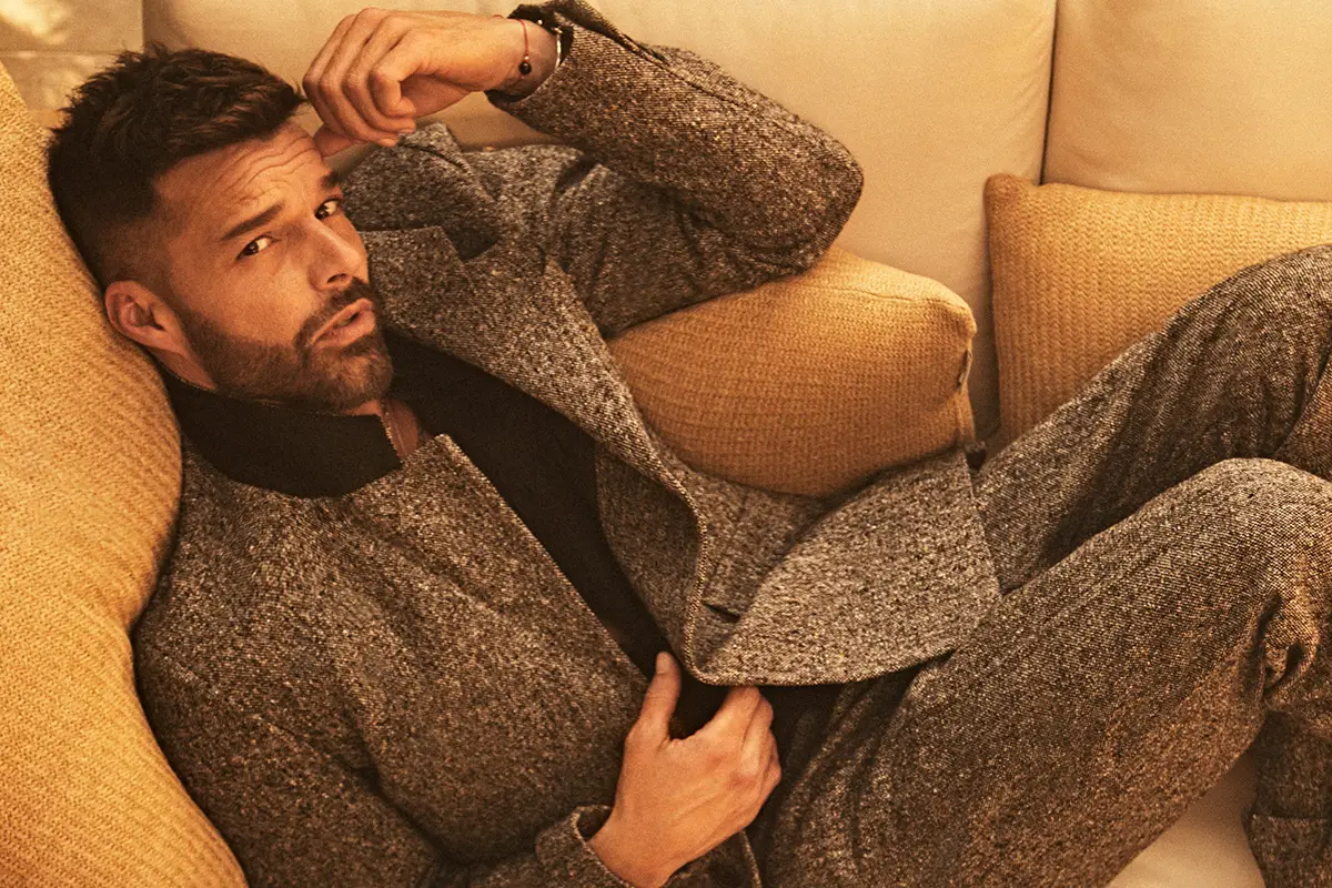 Ricky Martin posa en su casa de Los Ángeles. El cantante puertorriqueño se le ve recostado en un sillón vistiendo un traje gris. 
