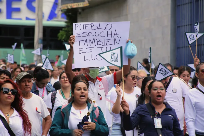 Un grupo de trabajadores sindicalizados del IMSS, vestidos de blanco y verde, marcha por calles de Cuernavaca con cárteles blancos y banderas del IMSS en demanda de aumento salarial, el 8 de octubre de 2026.