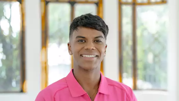 Foto medium shot de Prisca Awiti sonriendo, viste playera rosa mexicano con la bandera de México bordada, lleva cabello corto y aretes pequeños y discretos.