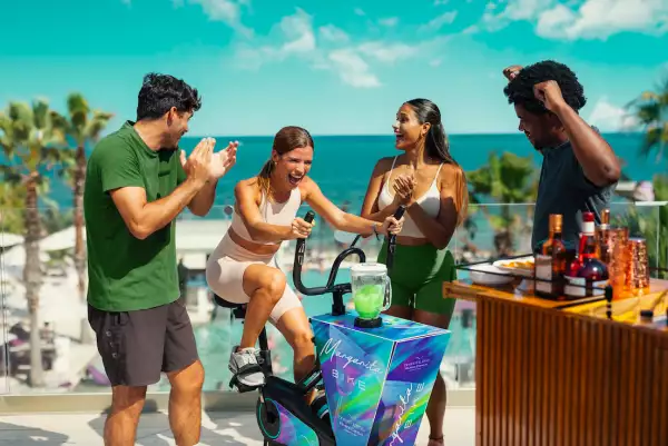 imagen de un grupo de amigos que se divierten preparando un coctel mientras una de ellos pedalea una bicicleta para activar la licuadora.