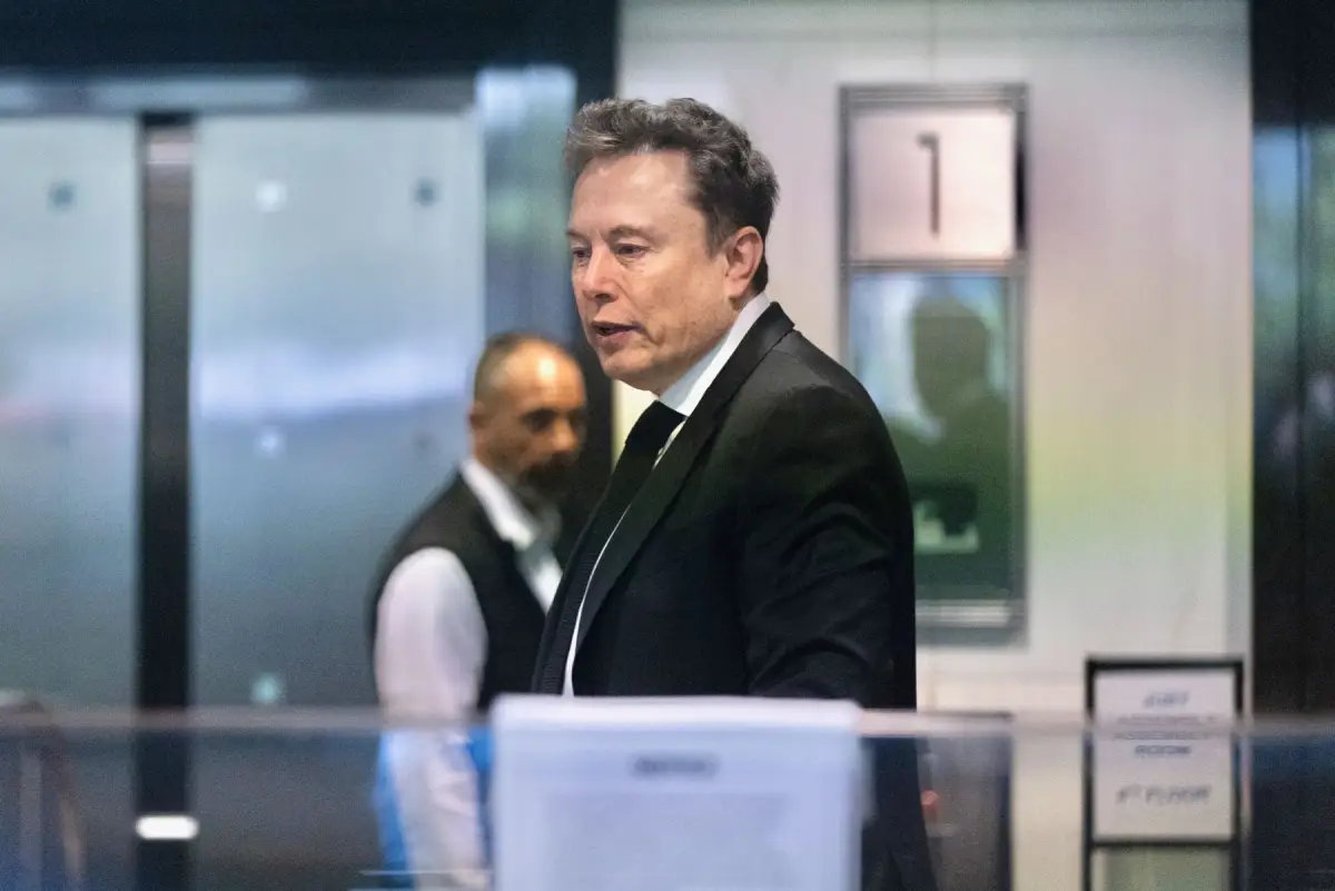 Elon Musk camina por el interior de un edificio mientras viste un traje negro y corbata.