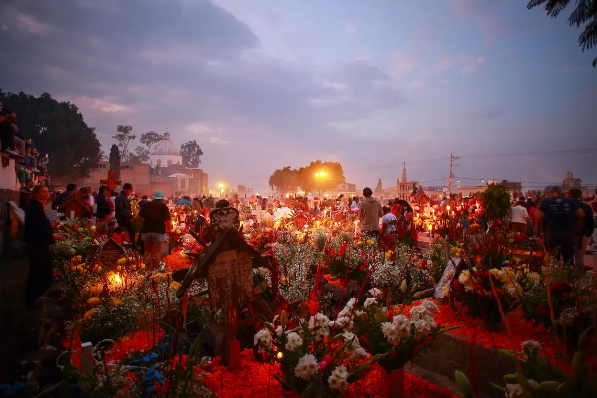 Foto del cementerio de Mixquic durante la noche del 2 de noviembre para celebrar el Día de Muertos, con tumbas iluminadas con velas y adornadas con miles de flores.