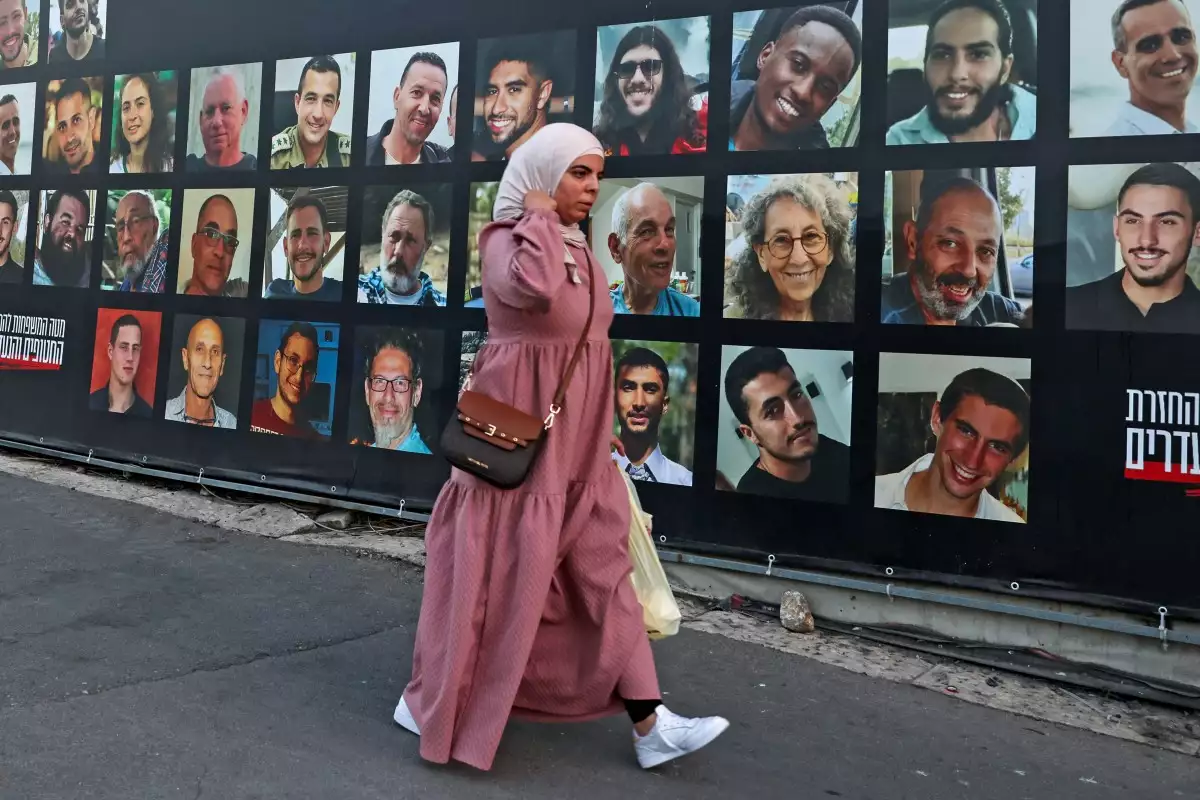 Una mujer pasa por una valla publicitaria con los retratos de israelíes retenidos como rehenes en la Franja de Gaza por militantes palestinos desde 2023, en Jerusalén el 6 de octubre de 2025.