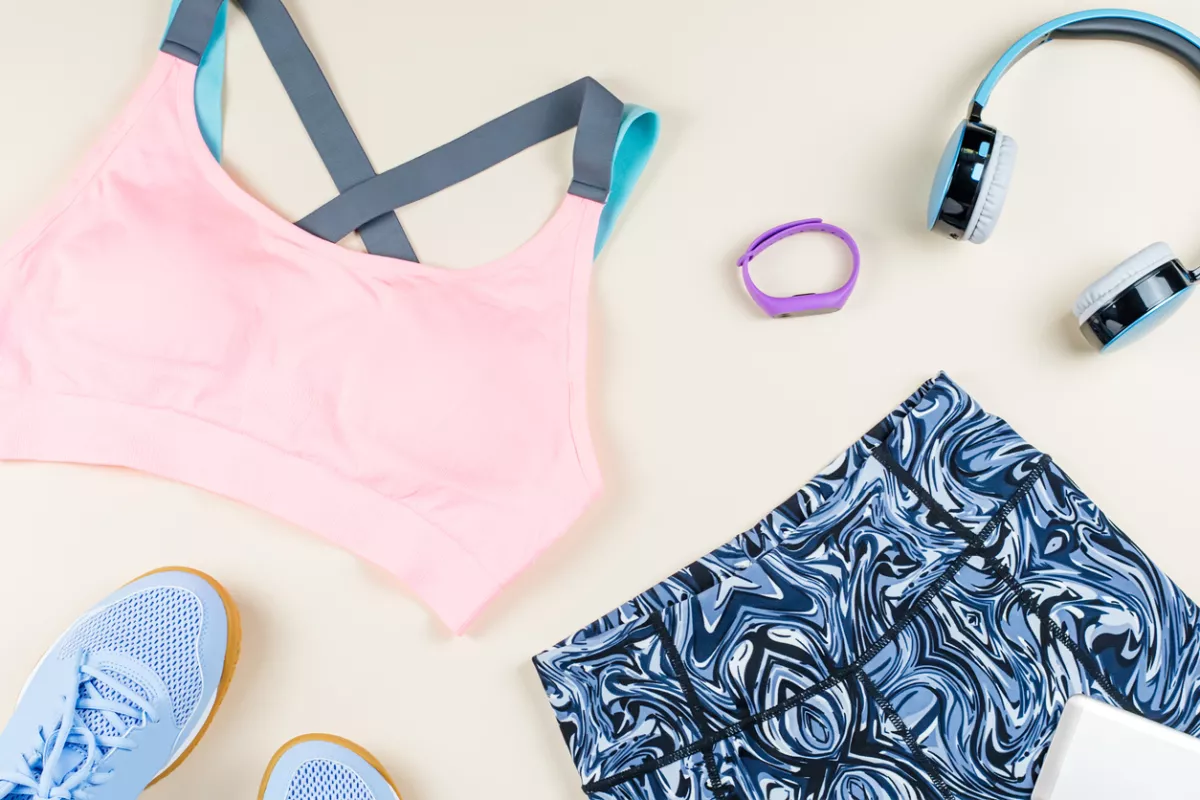 Woman sport bra, leggins, sneakers, headphones and fitness tracker on neutral background. Sport fashion concept.