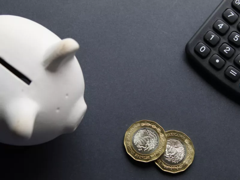 Monedas mexicanas entre una alcancía y una calculadora.