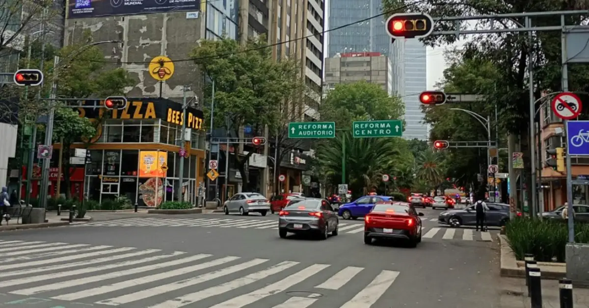 Dos carros circulan sobre una avenida de la CDMX. Hay semáforos y en la esquina del lado izquierdo hay una pizzeria.jpg