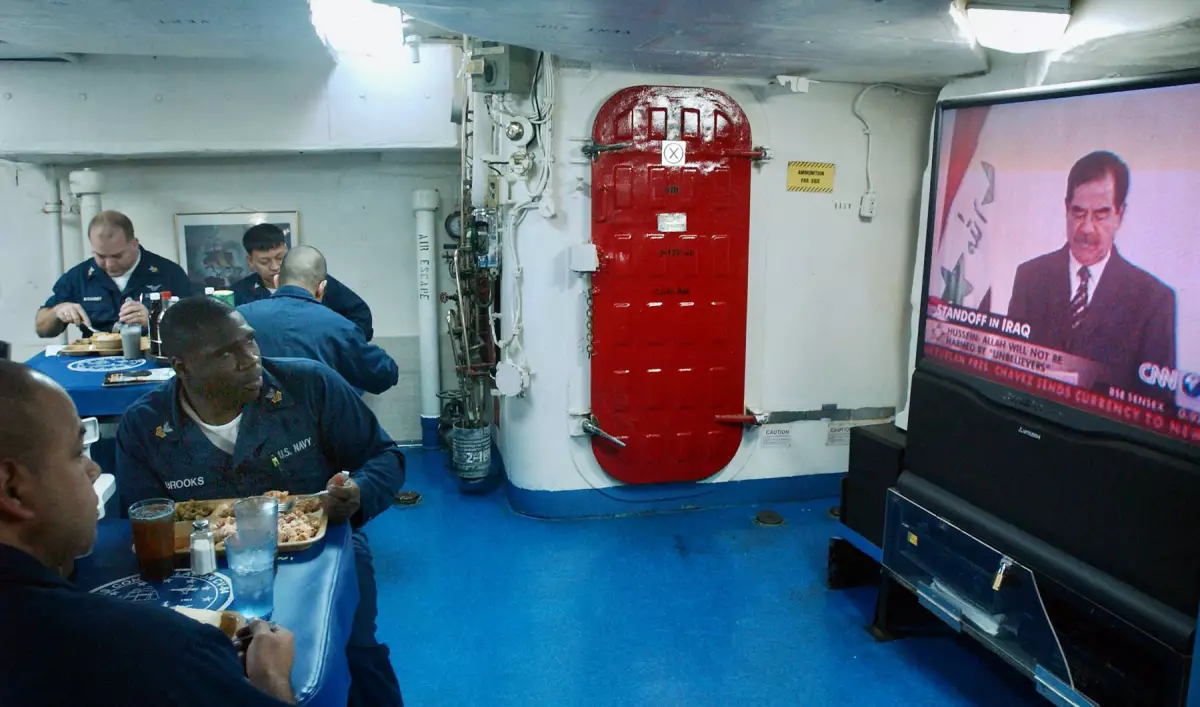 Los marineros a bordo del portaaviones de la Marina de los Estados Unidos USS Constellation almuerzan mientras ven un discurso televisado del presidente iraquí Saddam Hussein durante una patrulla del 17 de enero de 2003 en el Golfo Pérsico.