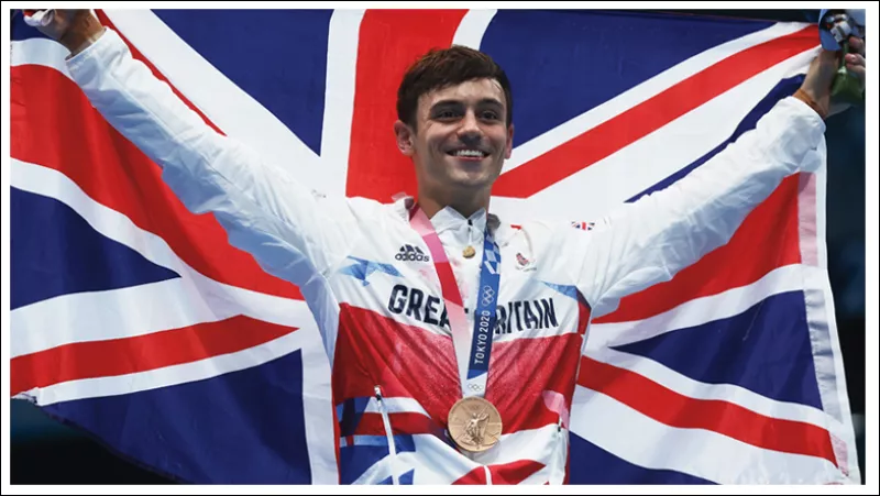 Foto de Tom Daley en Tokio 2020 con la bandera de Reino Unido detrás y su medalla olímpica colgando.