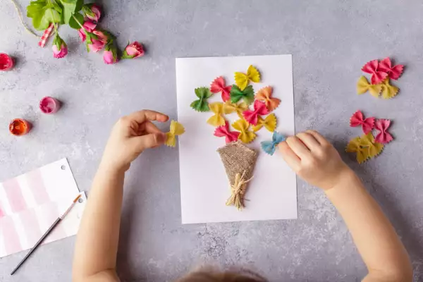 Manualidades en papel para el día de la madre o cumpleaños. Niño pequeño haciendo un ramo de flores de papel de colores y pasta de colores para mamá. Idea de regalo sencilla. copie el espacio