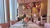 Una mesa con manteles blancos y un arreglo de rosas de diferentes tonalidades de rosa. Al fondo una Hello Kitty y arriba un letrero en color dorado con las palabras Hello Kitty Café.