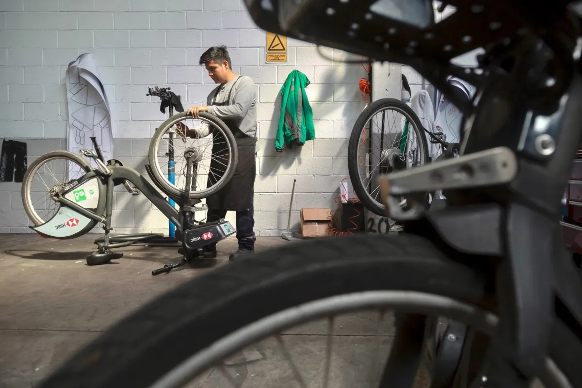 Un hombre repara una bicicleta de Ecobici. 