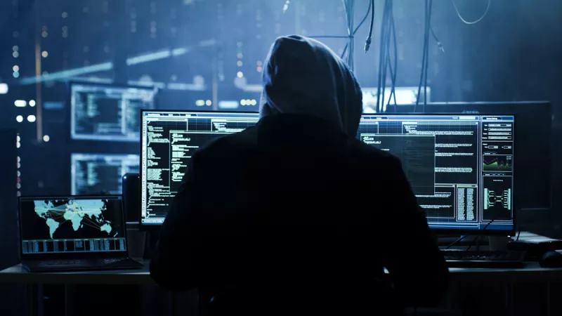 Dangerous Hooded Hacker Breaks into Government Data Servers and Infects Their System with a  Virus. His Hideout Place has Dark Atmosphere, Multiple Displays, Cables Everywhere.